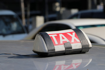 Taxi light sign or cab sign in white and red color with white text and tied with black tape on the car roof at the street.