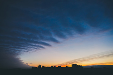 Cityscape with wonderful varicolored vivid dawn. Amazing dramatic blue cloud sky above dark...