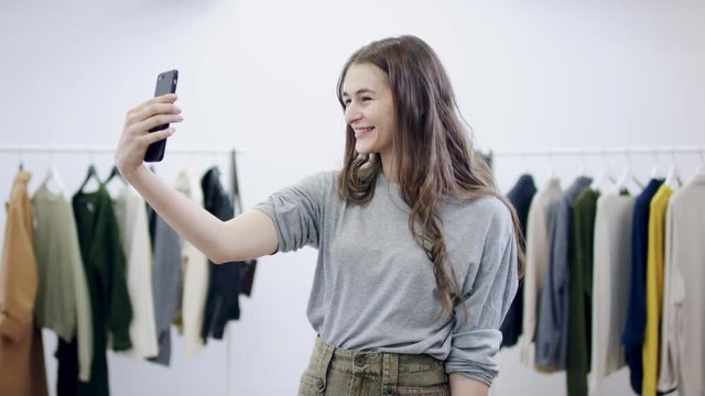 Cheerful young woman takes photos of herself on smartphone camera in a clothing room