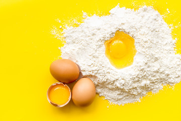 Making dough concept. Pile of flour and eggs on yellow background top view space for text