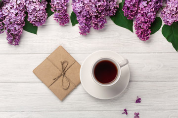 A bouquet of lilacs with cup of tea and craft envelope on white boards