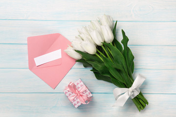 A bouquet of white tulips with a gift box, love note and color envelope on blue wooden boards