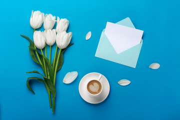 White tulips with petals, cup of coffee, a love note and color envelope on a blue background