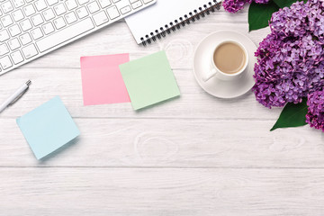 Office desktop with a bouquet of lilacs, coffee cup, keyboard, notebook and colored stickers on white boards