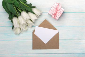 A bouquet of white tulips with a gift box, love note and envelope on blue wooden boards