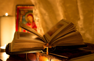 The light from the burning candles falls on the Bible, which lies on a dark background, there is an...