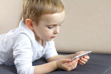 Fototapeta premium Cute little boy using smartphone voice application at home. Happy smart child using mobile app. Education, technology and fun concept.