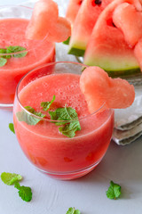 Glasses of fresh watermelon juice or smoothie decorated mint leaves and watermelon slices on gray wooden background. Copy space