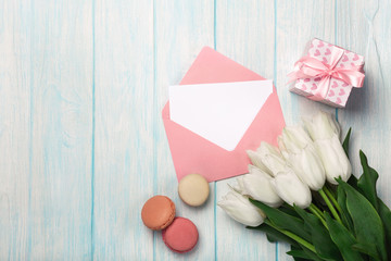 A bouquet of white tulips with a gift box, macarons, love note and color envelope on blue wooden boards