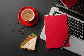 Obraz na płótnie Canvas Elegant black office desktop with laptop, cup of coffee and a sandwich for lunch. Top view with copy space