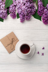 A bouquet of lilacs with cup of tea and craft envelope on white boards