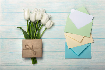 A bouquet of white tulips with a love note and color envelopes on blue wooden boards