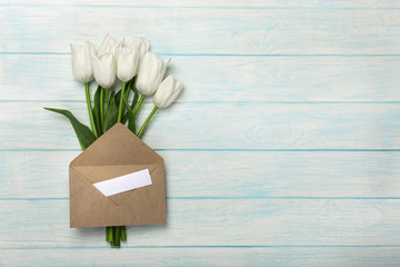 A bouquet of white tulips with a love note and envelope on blue wooden boards