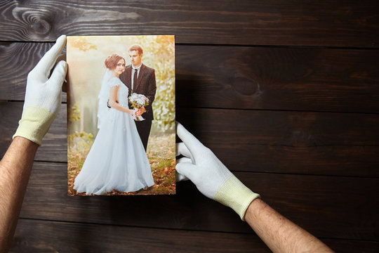 Photo of a wedding couple printed on canvas. Male hands in white gloves hold a photography with gallery wrapping on stretcher bar