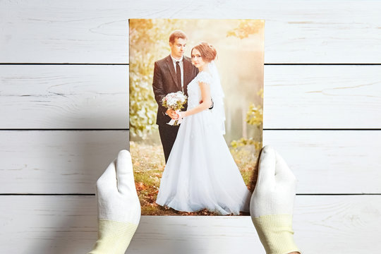 Photo of a wedding couple printed on canvas. Male hands in white gloves hold a photography with gallery wrapping on stretcher bar