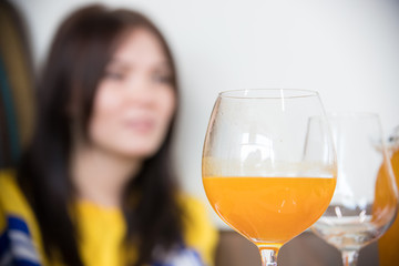 Group of young friends sitting in cafe. A glass with orange drink on a foreground