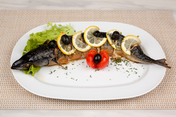 Stuffed fish with lemon and olives on a white dish.