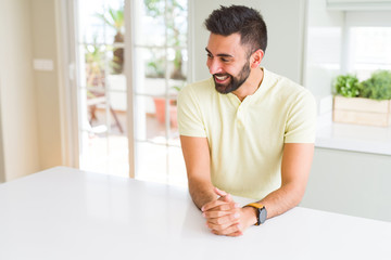 Handsome hispanic man casual yellow t-shirt at home looking away to side with smile on face, natural expression. Laughing confident.