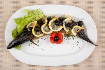 Stuffed fish with lemon and olives on a white dish.