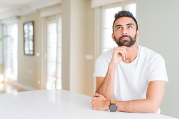 Handsome hispanic man casual white t-shirt at home with hand on chin thinking about question, pensive expression. Smiling with thoughtful face. Doubt concept.