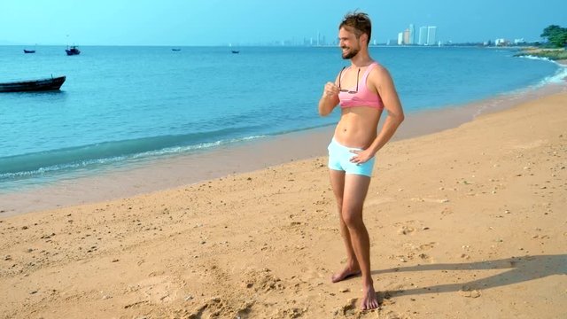 Playful handsome guy in a pink t-shirt and blue shorts rejoices at the beach. freak on the sea.