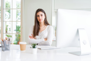 Beautiful young woman working using computer skeptic and nervous, disapproving expression on face with crossed arms. Negative person.