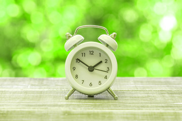 Alarm clock, clock on a wooden table on a background of vegetation.  time, business planning.