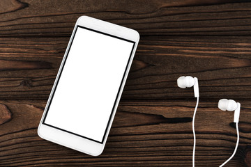 Mobile phone with white screen, headphones on wooden table background.  Internet, listening to sounds.
