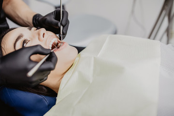 Dentist examining patient teeth with a mouth mirror and dental excavator. Close-up view on the woman face