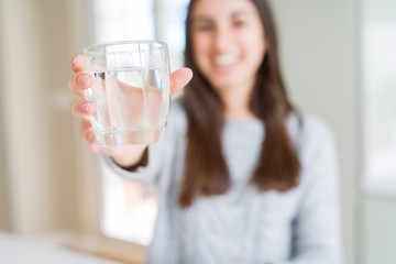 Beautiful young woman drinking a fresh glass of water with a happy face standing and smiling with a confident smile showing teeth