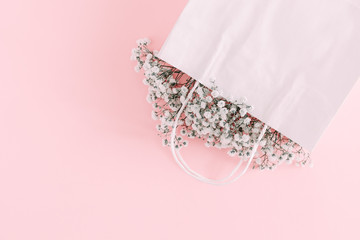 Flowers composition minimal. White flowers gypsophila in white paper bag on pastel pink background....