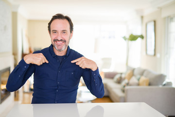 Fototapeta premium Handsome middle age man at home looking confident with smile on face, pointing oneself with fingers proud and happy.