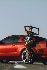 beautiful young woman with long dark hair in shorts sitting on the fender of red car on the sunset