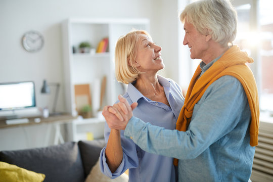 Side view portrait of loving senior couple dancing at home, copy space