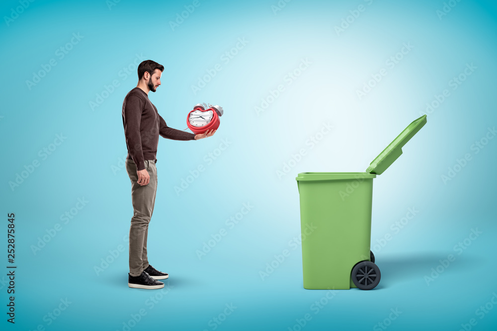 Poster man throwing broken red clock into open trash bin on blue background