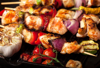 Grilled chicken skewers with spices and vegetables in a pan on black background