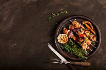 Grilled chicken skewers with spices and vegetables in a pan on dark background