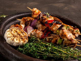 Grilled chicken skewers with spices and vegetables in a pan on dark background