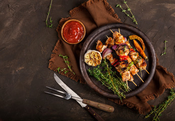 Grilled chicken skewers with spices and vegetables in a pan on dark background