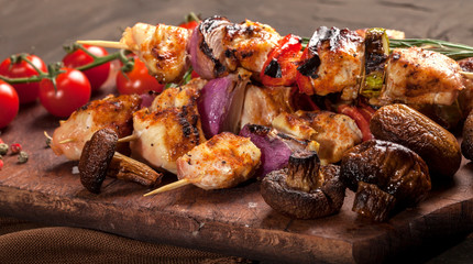 Grilled chicken skewers with spices and vegetables on cutting board and dark background