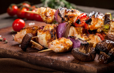 Grilled chicken skewers with spices and vegetables on cutting board and dark background
