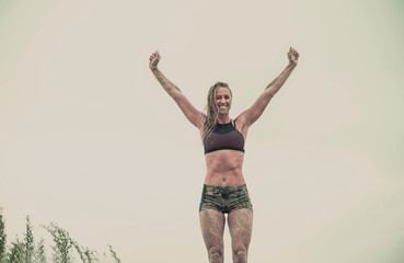 Strong athletic woman with mud on her face and body after running in rain or extreme sport...