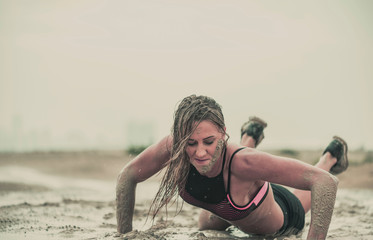Closeup of strong athletic woman crawling in wet muddy puddle with mud on her face in an extreme...