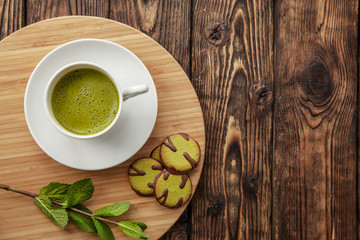 cup of Matcha tea and green cookies on a round wooden tray