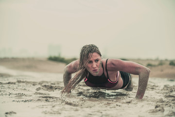 Closeup of strong athletic woman crawling in wet muddy puddle with mud on her face in an extreme competitive sport