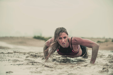 Closeup of strong athletic woman crawling in wet muddy puddle with mud on her face in an extreme competitive sport