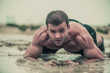 Closeup of strong athletic, muscular man crawling in wet muddy puddle in the rain in an extreme...