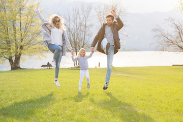 Fototapeta premium Happy father, mother and little girl jumping near lake on a beautiful sunny day.