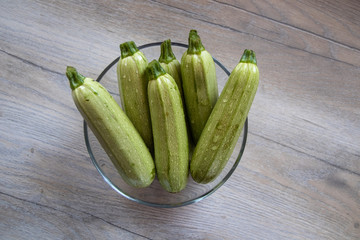 Light green zucchini in a glass bowl on white wooden table