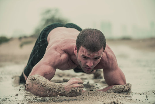 Closeup of strong athletic, muscular man crawling in wet muddy puddle in the rain in an extreme competitive sport 